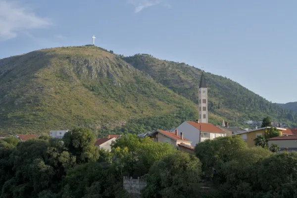 Mostar avec un clocher et une croix sur la colline à l'heure crépusculaire.