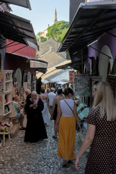 Vue portrait d'une rue animée de la vieille ville de Mostar au crépuscule, avec un pavé de pierres et une architecture historique.