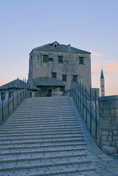 Le Vieux Pont (Stari Most) à Mostar à l'aube, avec des marches en pierre et des bâtiments historiques en arrière-plan.