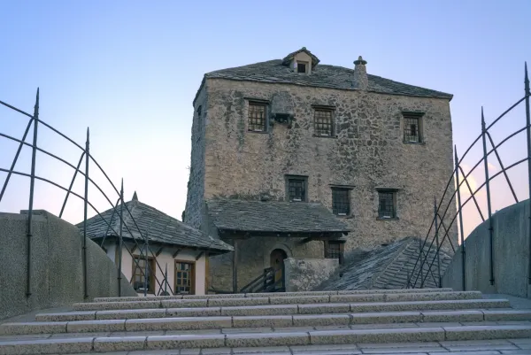 An ancient stone tower and adjacent buildings at the Old Bridge in Mostar, Bosnia and Herzegovina, featuring stone steps.