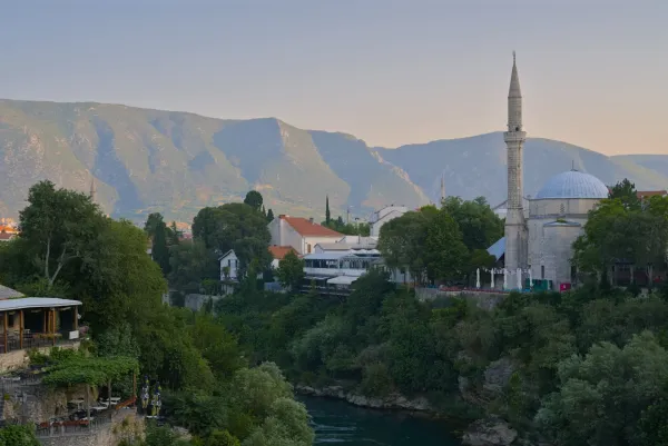 Fotografía paisajística de Mostar en la hora dorada, con el río, una mezquita y montañas.