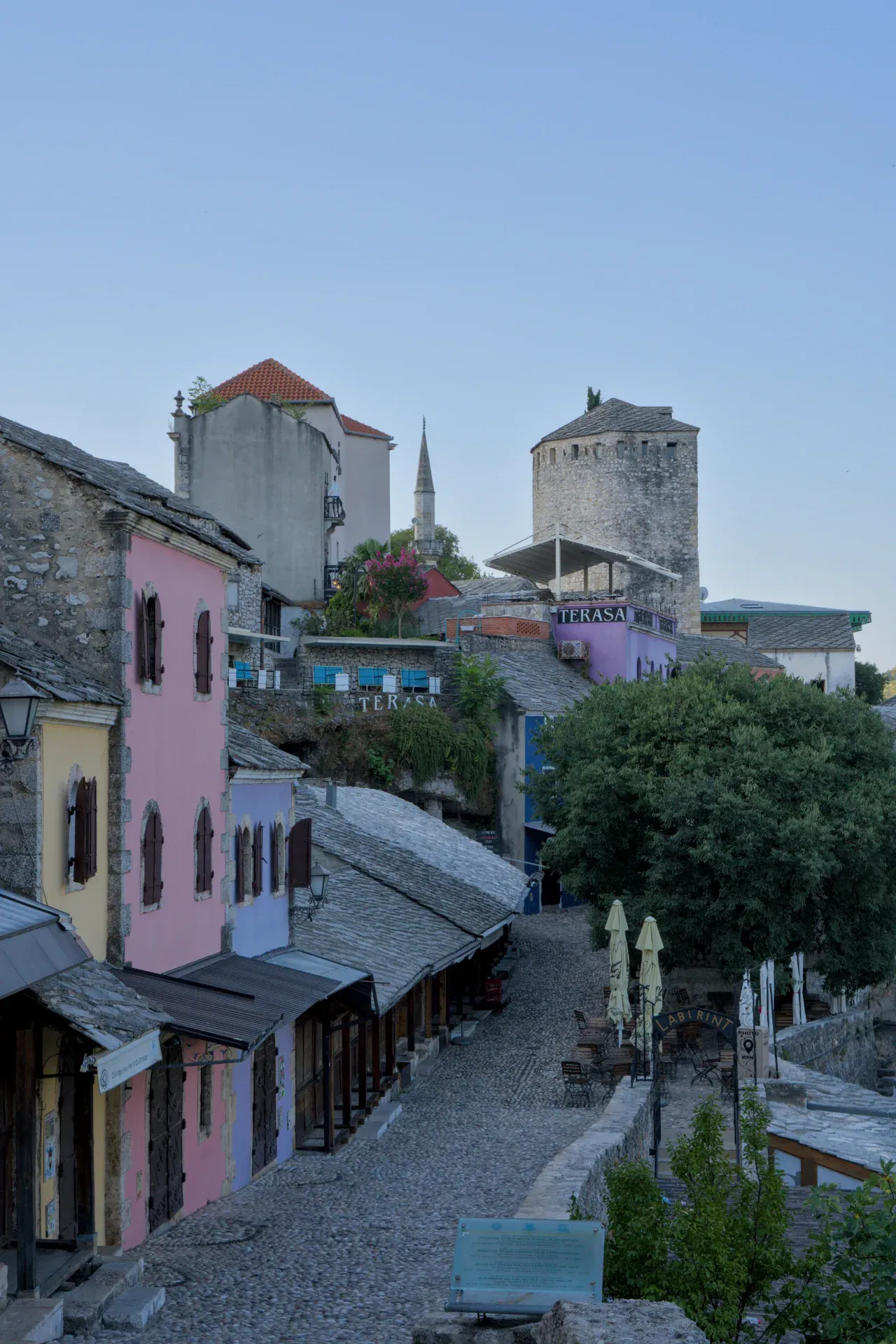 Svanuće nad istorijskim Starim Gradom Mostara u Bosni i Hercegovini, sa šarenim zgradama i kaldrmisanim ulicama.