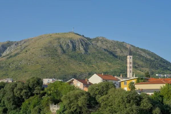 Paysage artistique panoramique de Mostar avec une grande croix sur la colline et un clocher d'église élancé au premier plan.