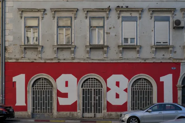 Graffiti "1981" on a red wall in Mostar, Bosnia and Herzegovina, with historical windows and facade details.