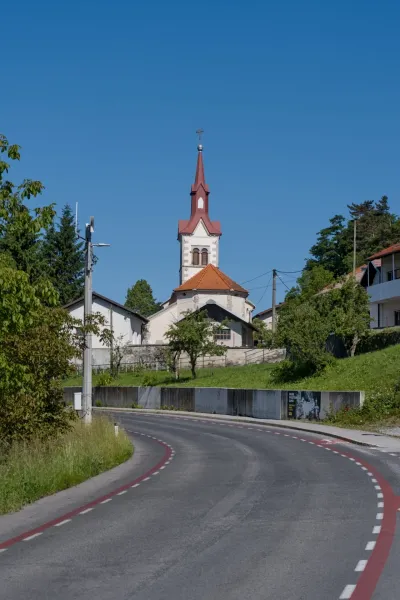 Une route sinueuse mène à une église avec une imposante flèche rouge à Predjama, Slovénie, sous un ciel bleu clair.