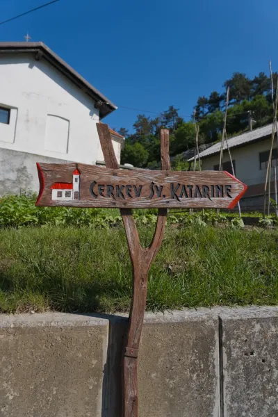 A wooden signpost reading 'CERKEV SV. KATARINE' points the direction to the church on the way to Predjama.