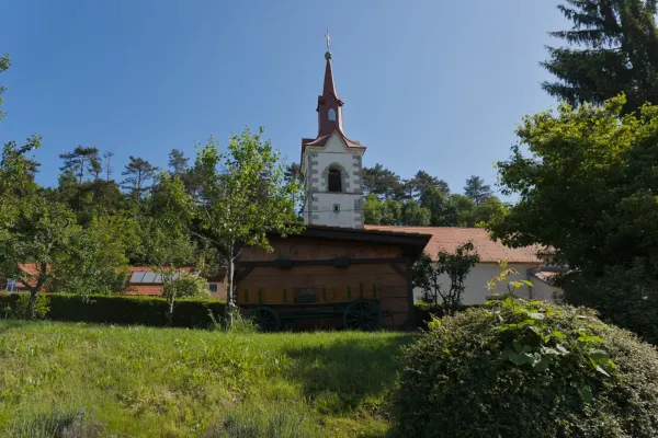 Picturesque village church with a red bell tower and a wooden shed with an old cart, on the way to Predjama Castle, Slovenia.