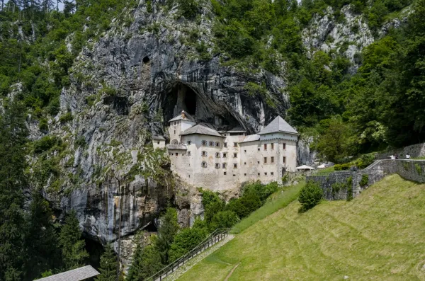 Le château historique de Predjama s'élève majestueusement d'une falaise verticale en Slovénie, entouré d'une verdure luxuriante.