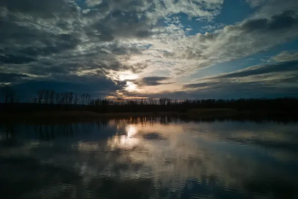 Dramatischer Sonnenuntergang über dem Wasser an der Begečka Jama bei Novi Sad mit Wolken und Reflexionen.
