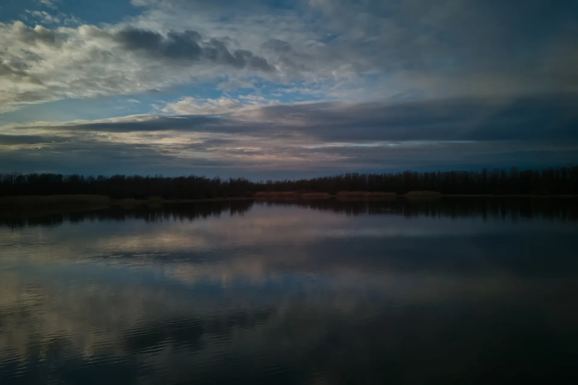 Begečka Jama before sunset, featuring dramatic clouds reflected on calm water surface.