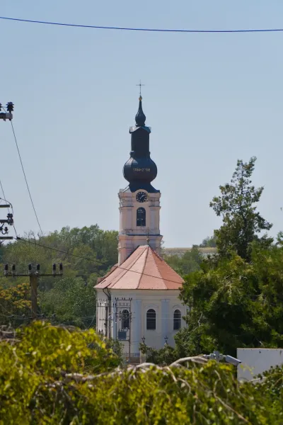 Photographie de portrait d'une église à Irig, Serbie, avec une tour et un toit distinctifs, sur un ciel bleu clair.