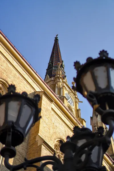Photo de l'Église de la Vierge Marie à Novi Sad, Serbie, avec un toit en tuiles et une horloge, prise en contre-plongée.
