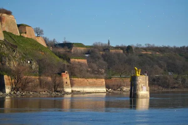 Steinmauern der Peterwardeiner Festung ragen über dem blauen Wasser der Donau unter klarem Himmel auf und schaffen eine historische Landschaft.