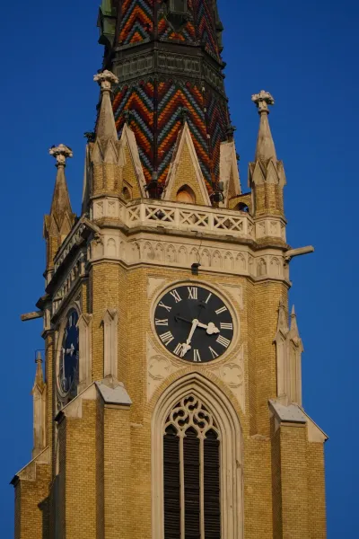 Primer plano del reloj en la torre de la Iglesia de la Virgen María en Novi Sad, Serbia, con números romanos en una esfera oscura.