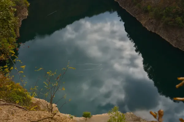Zwei Enten gleiten gemächlich über die spiegelglatte Oberfläche des Ledinačko-Sees und spiegeln die Wolken wider. Blick von der Felswand.
