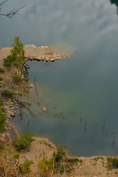 Ein Boot am Ledinačko-See am frühen Morgen, das Wolken im ruhigen Wasser spiegelt.