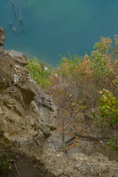 Blick von einer hohen, steilen Klippe auf den Ledinačko See, Serbien, mit türkisfarbenem Wasser und herbstlichen Bäumen.