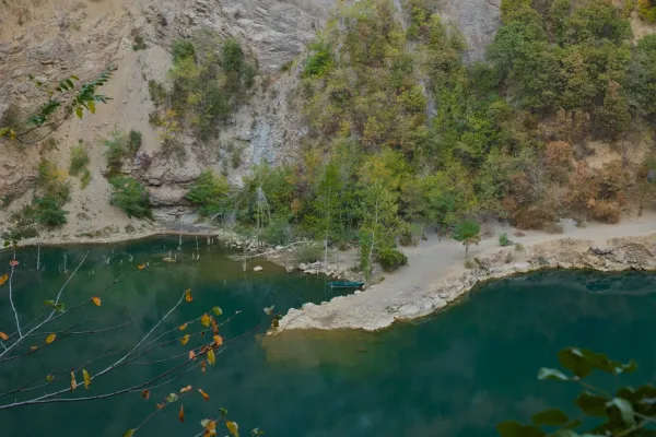 Kleines Boot am felsigen Ufer des Ledinačko-Sees, umgeben von Bäumen und Felsen.