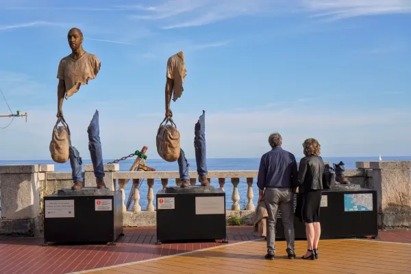 Une collection de tours en pierre et de bâtiments résidentiels est nichée sur une colline densément boisée à Gênes, Italie, sous un ciel bleu vif.