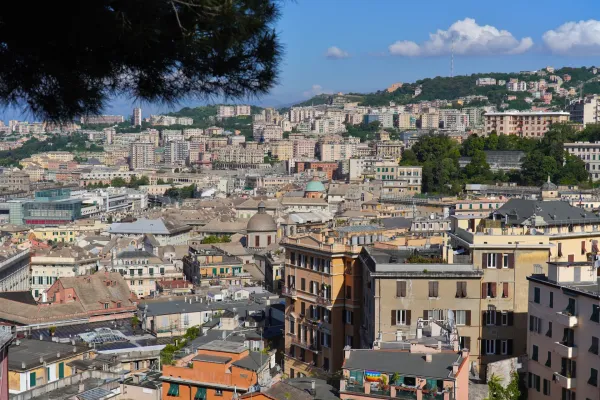 Vue sur des bâtiments colorés et des arbres verts sur les collines de Gênes, Italie, avec une tour historique en arrière-plan sous un ciel bleu éclatant.
