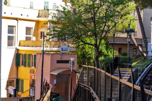 Pogled na zgradu stanice Funicolare San Nicola u Đenovi, Italija, sa fasadom boje breskve, modernim liftom i signalizacijom za Funicolare Zecca – Righi.