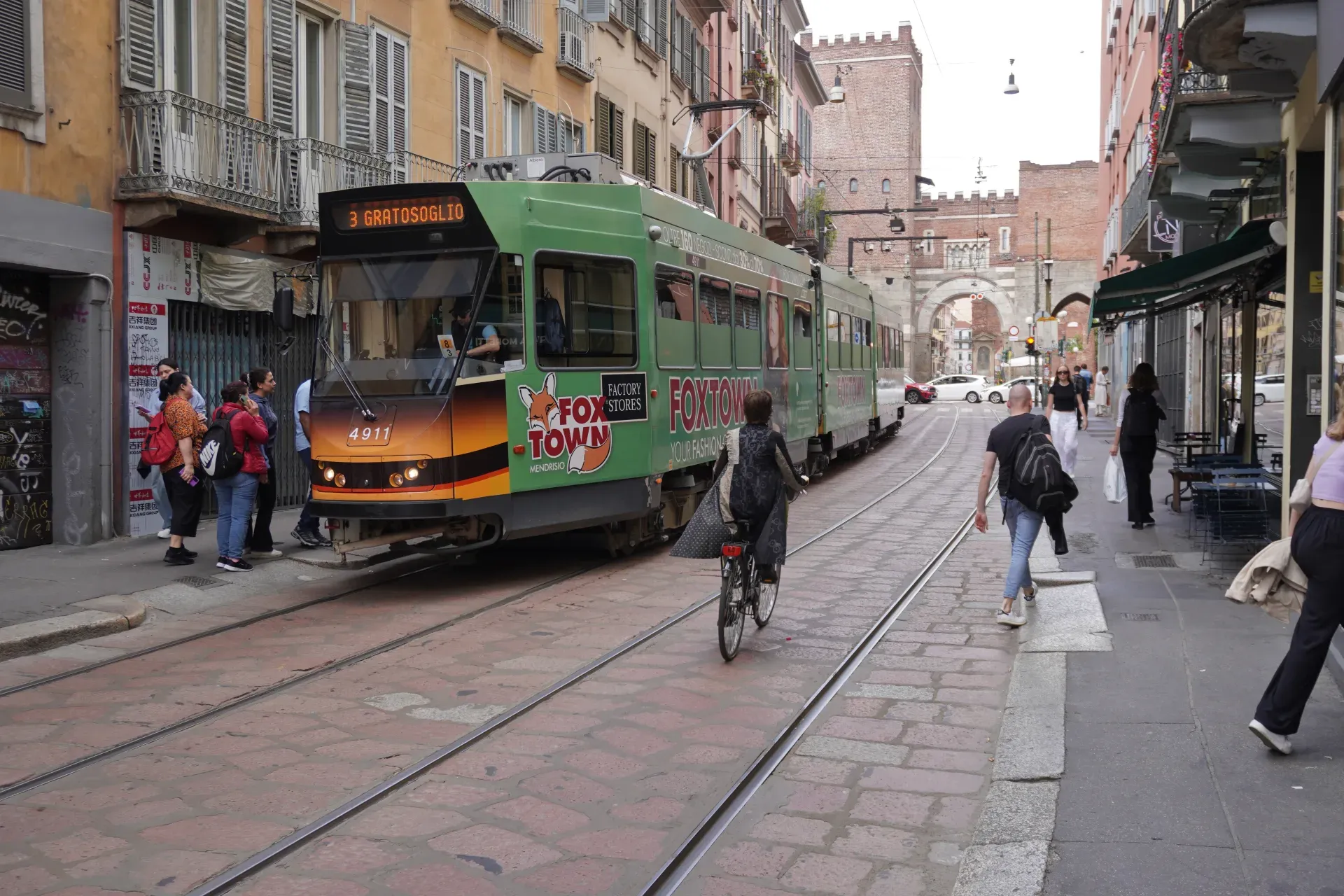 Tranvía amarillo en una calle empedrada de Milán con edificios y cafés a los lados.