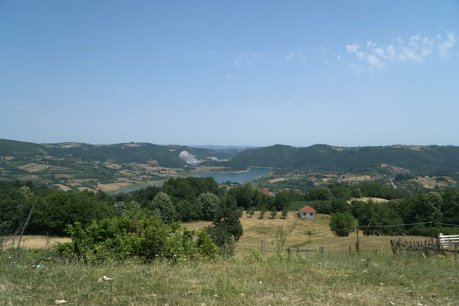 A rolling landscape with a lake and green trees, on the way to Tara National Park in Serbia, with a small house in the distance.