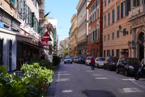 Street view of Via Balbi in Genoa Italy with historic buildings and parked cars under a blue sky.