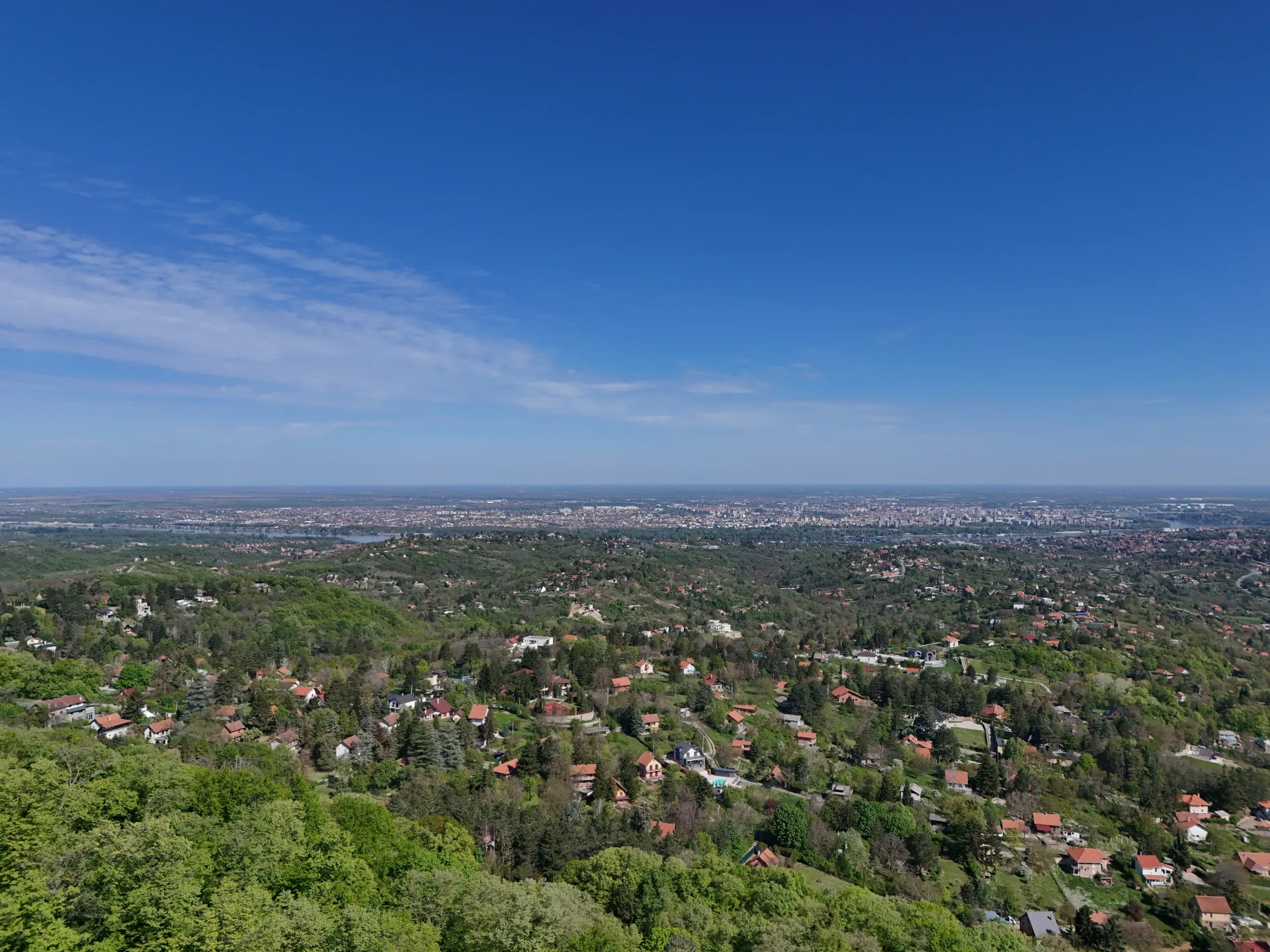A bird's-eye view of Novi Sad, Serbia, showing a city landscape with hills, houses, and the sky.