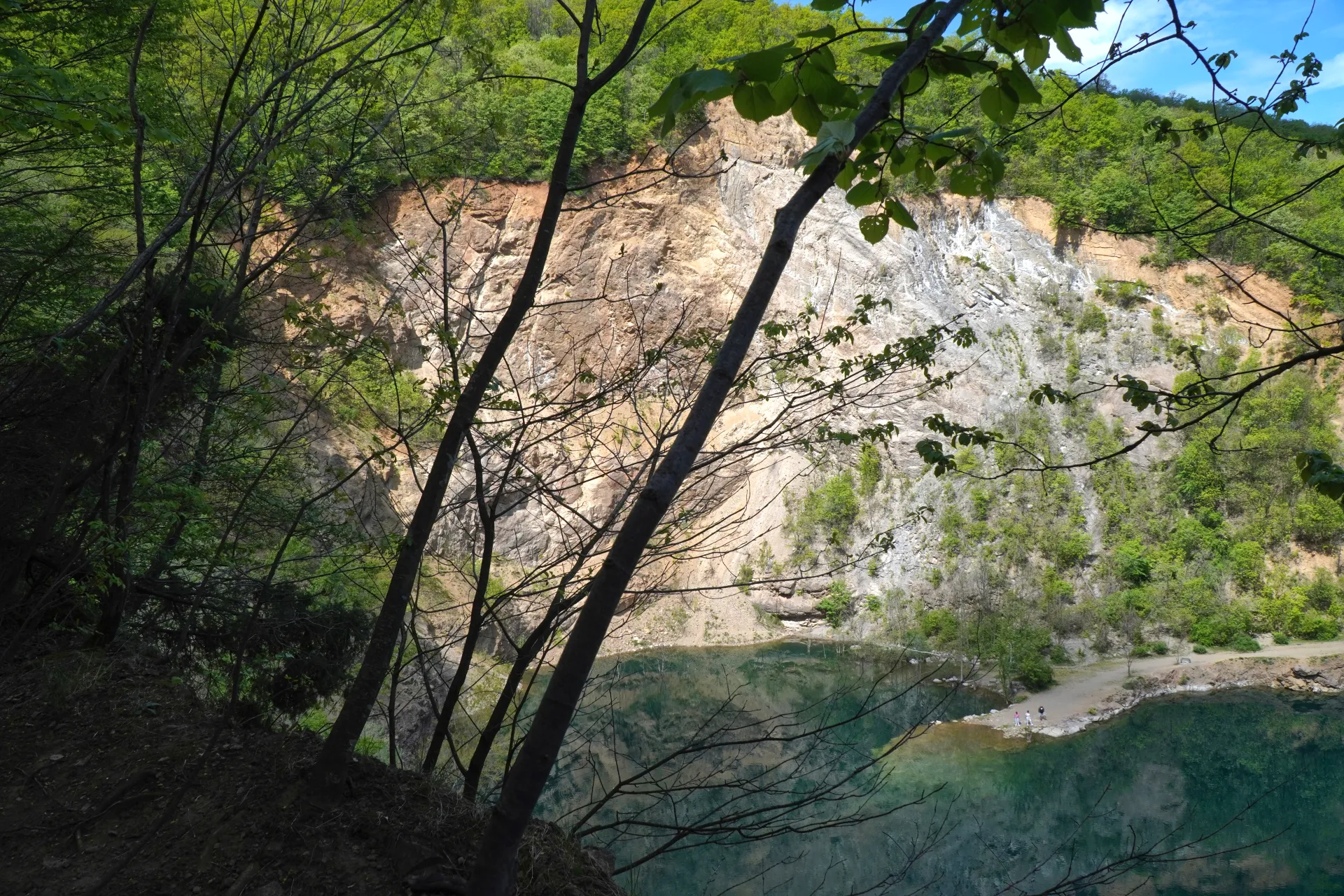 Ledićko Lake in Novi Sad, Serbia, with clear blue-green water and rocky shores framed by trees.