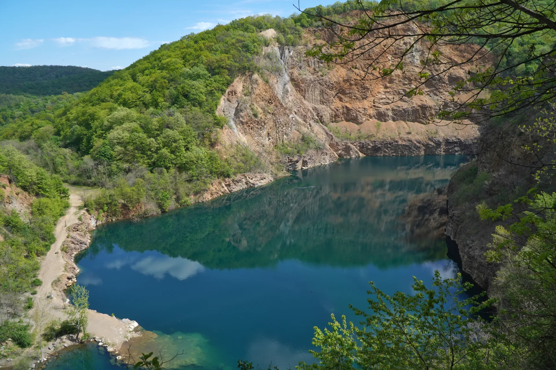 Ízvanredno plavo jezero, Ledinačko jezero (Ledinačko jezero), smešteno u bivšem kamenolomu u blizini Novog Sada, Srbija, sa bujnim zelenim drvećem i stenovitim liticama koje okružuju njegove mirne vode.