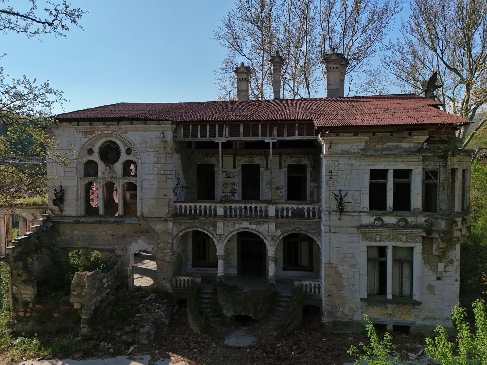 Vazdušni pogled na napušteni Dvorac Špicer u Beočinu, Srbija, prikazujući njegovu urušavajuću arhitekturu i zaraslo okruženje pod vedrim plavim nebom.