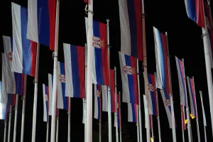 Numerous Serbian flags with their coat of arms flying on flagpoles against a dark night sky in Novi Sad.