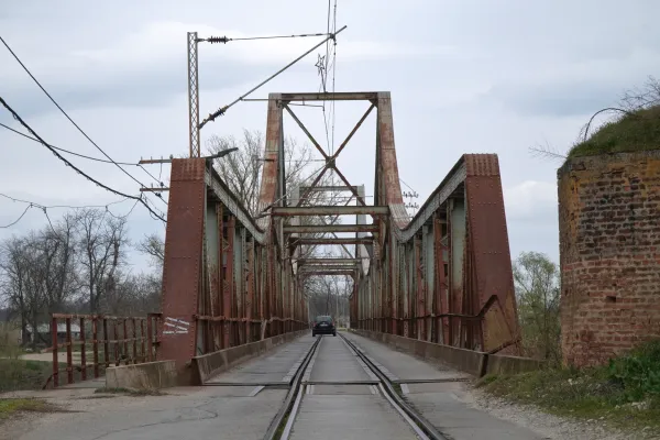 The Ljubičevski Bridge, an iron bridge over the Morava River near Požarevac, Serbia, with a car driving on it, showing the rusty metal girders and tracks.