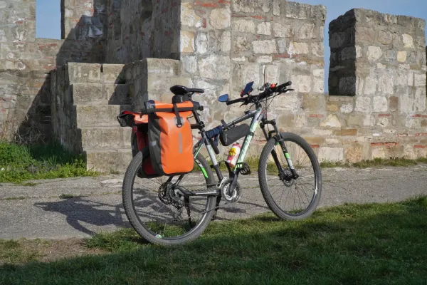 Un vélo chargé de sacoches orange se trouve sur un chemin pavé devant un ancien mur de pierre de la forteresse de Smederevo, Serbie.