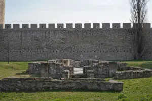 Ancient stone foundations and walls on the grass with the high stone wall of Smederevo Fortress in the background, Serbia.