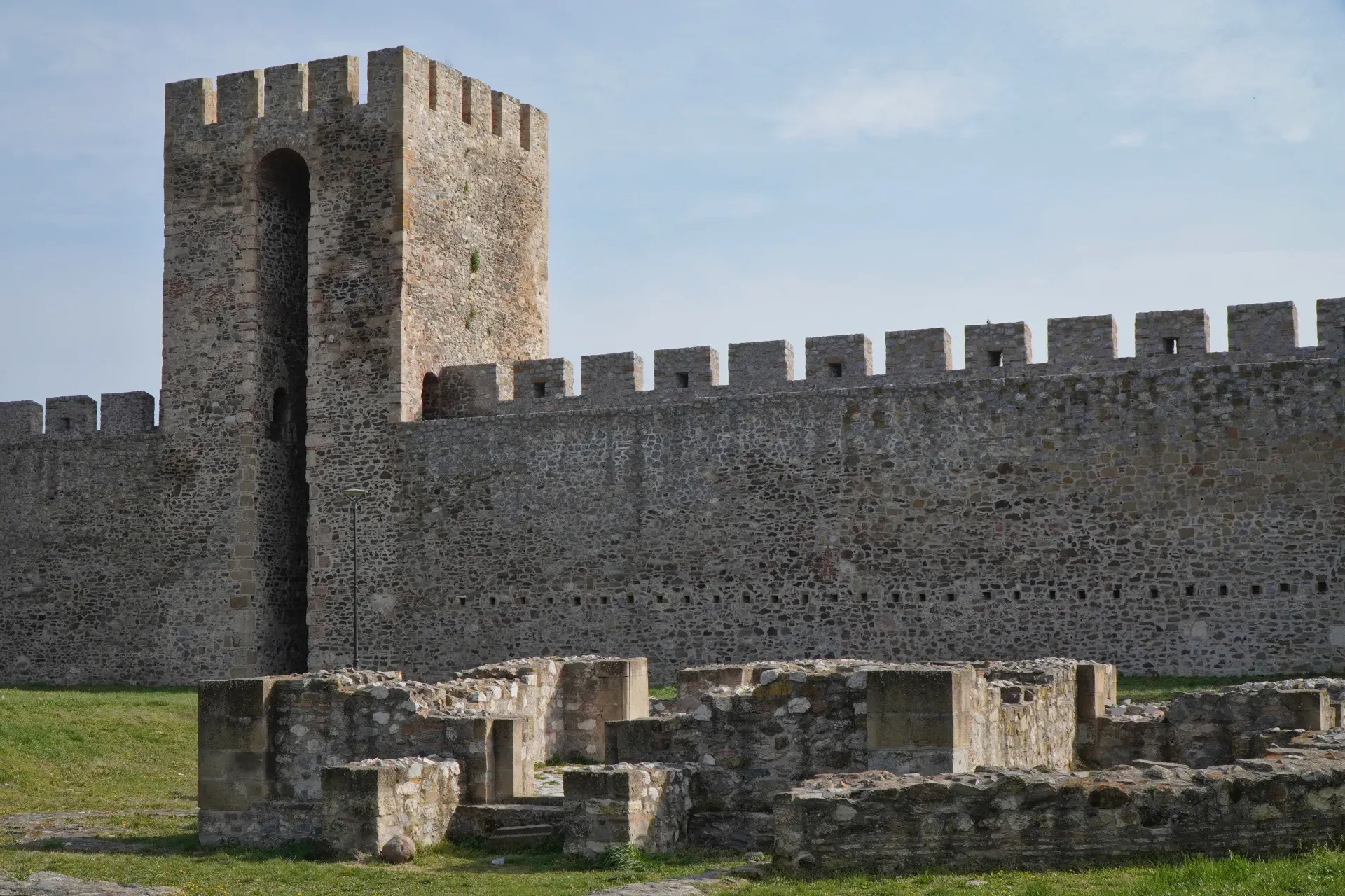 The ruins of a religious building are visible in front of the impressive stone wall and watchtower of Smederevo Fortress in Serbia.