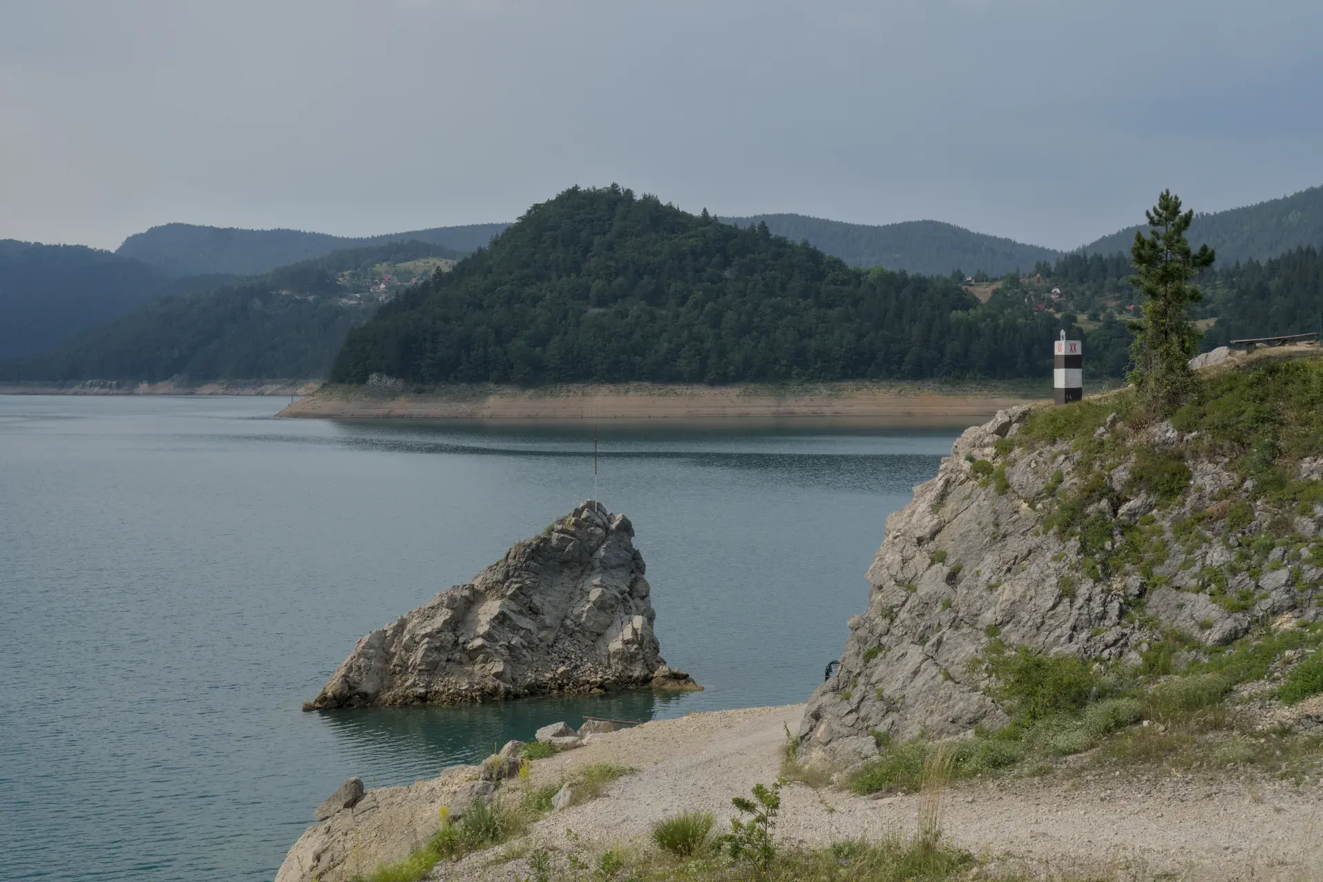 Zaovine Lake in Tara National Park, Serbia, with green mountains, rocks, and a lighthouse.