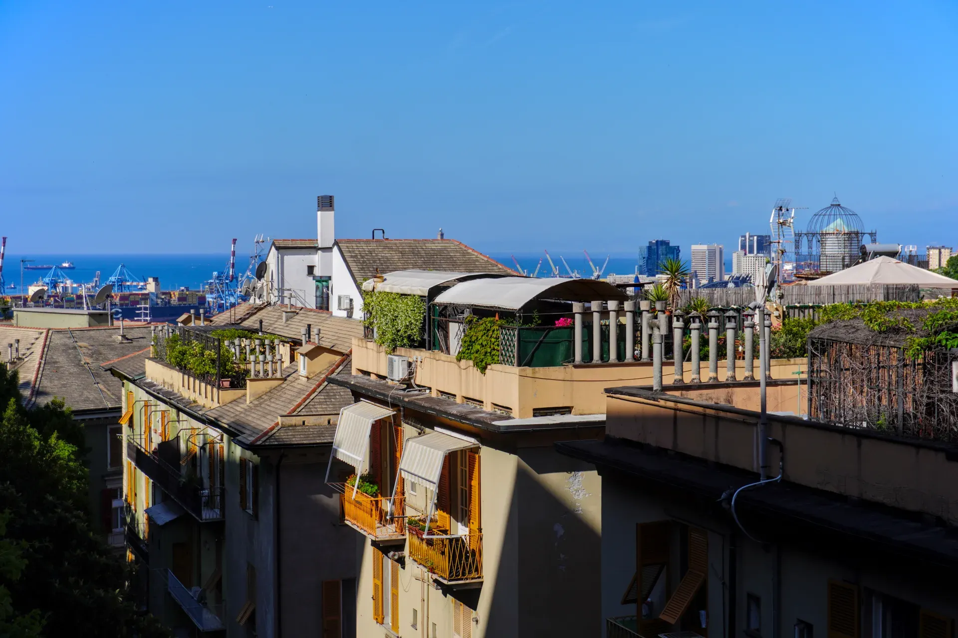 View over the rooftops of Genoa overlooking the port and the sea under a clear blue sky.