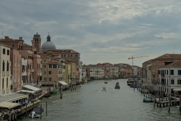 Grand kanal u Veneciji sa tradicionalnim zgradama pastelnih boja i čamcima na vodi, snimljen pod oblačnim nebom.
