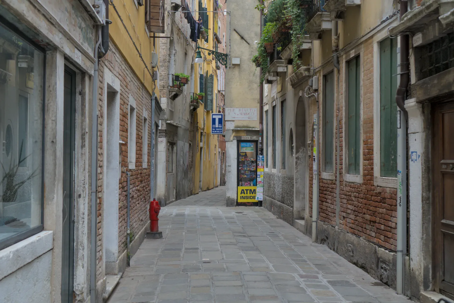 Photograph of a narrow Venetian alley with cobblestones, brick walls, and historic buildings.