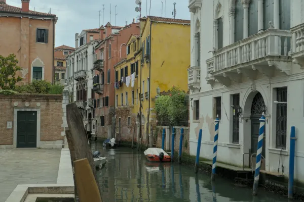 Mirni venecijanski kanal sa tradicionalnim šarenim kućama i reflektujućim površinama vode.