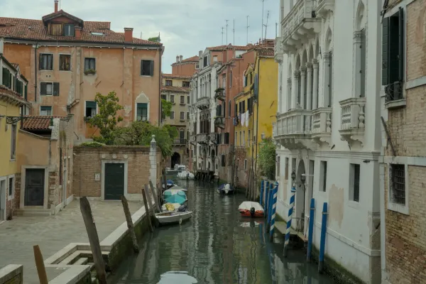 Uzak kanal u Veneciji sa istorijskim zgradama i nekoliko čamaca koji miruju na vodi.