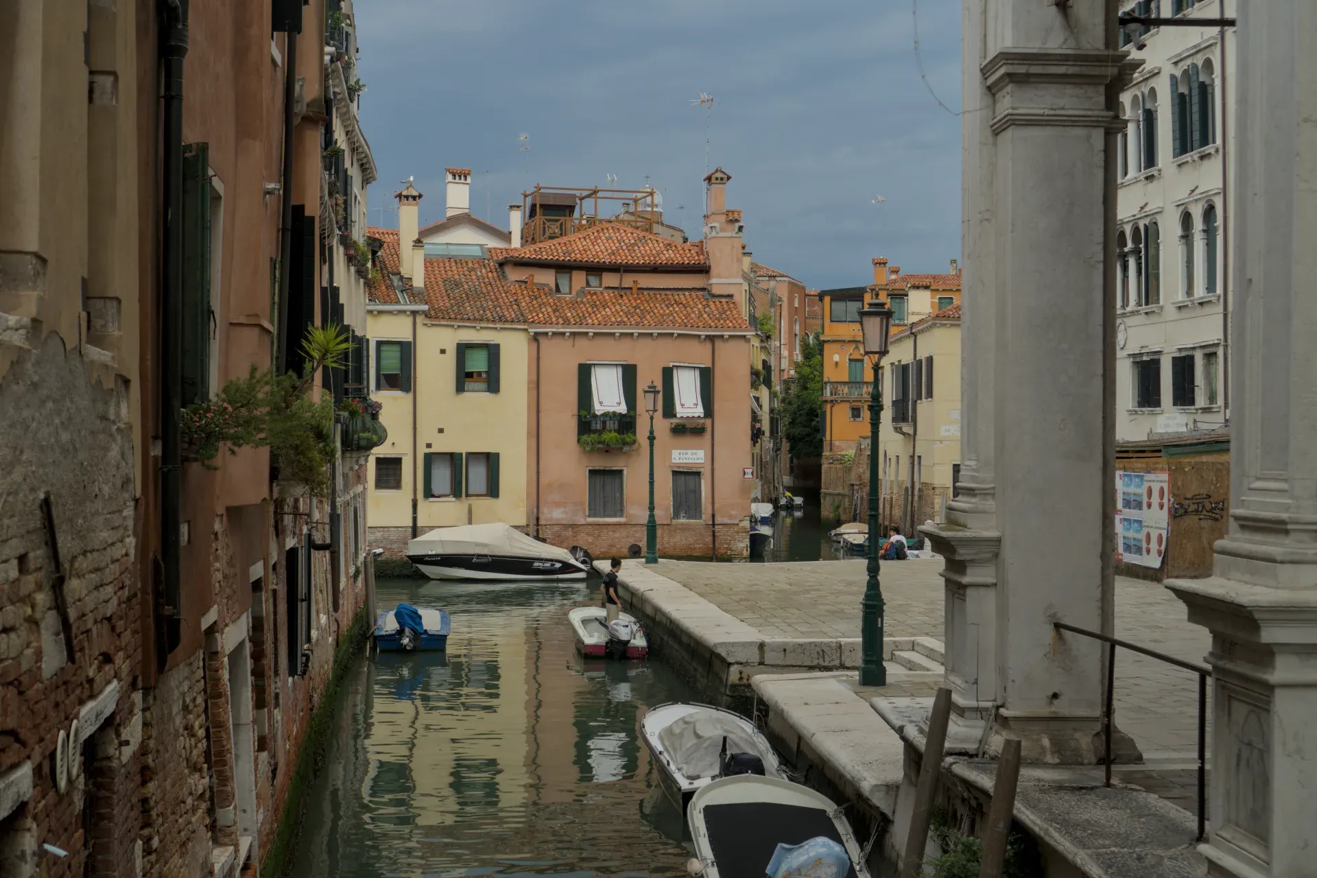 A Venice canal with various boats, surrounded by colorful historic buildings and a cloudy sky.