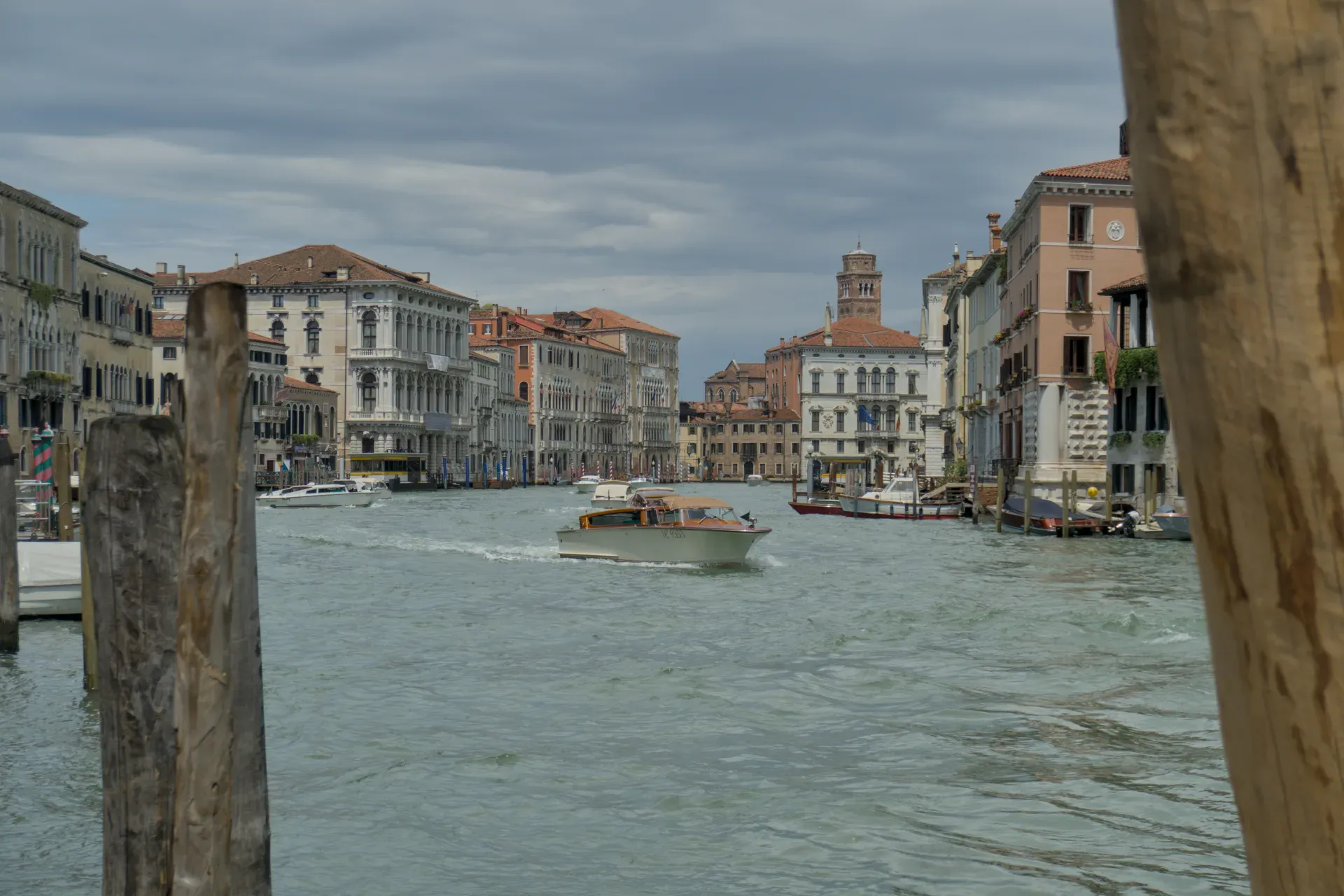Un bateau navigue sur le Grand Canal à Venise, entouré de bâtiments historiques sous un ciel nuageux.
