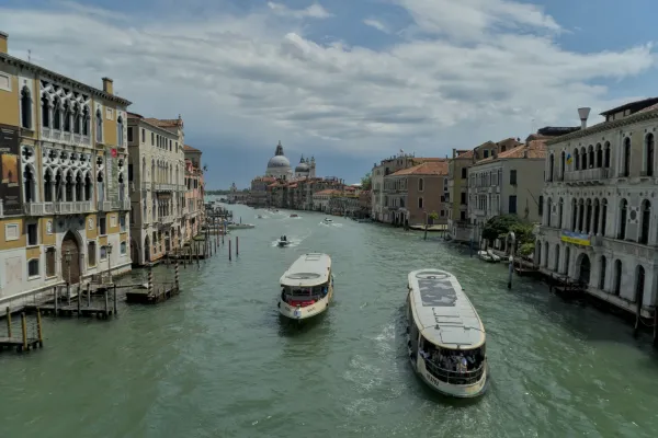 Zwei Boote fahren den Canal Grande in Venedig, flankiert von historischen Palästen und einer Kuppel im Hintergrund.