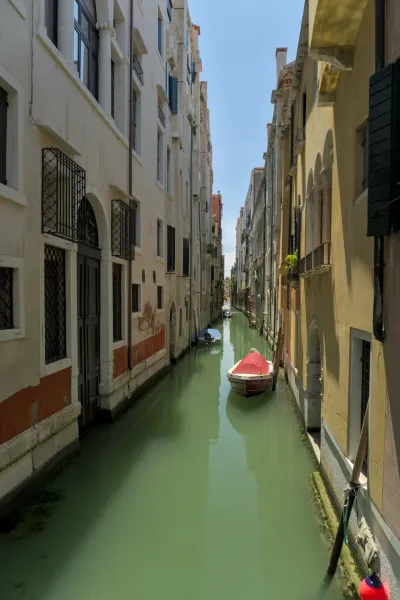 Užurbana venecijanska ulica sa čamcem u smaragdno zelenoj vodi, okružena istorijskim zgradama.