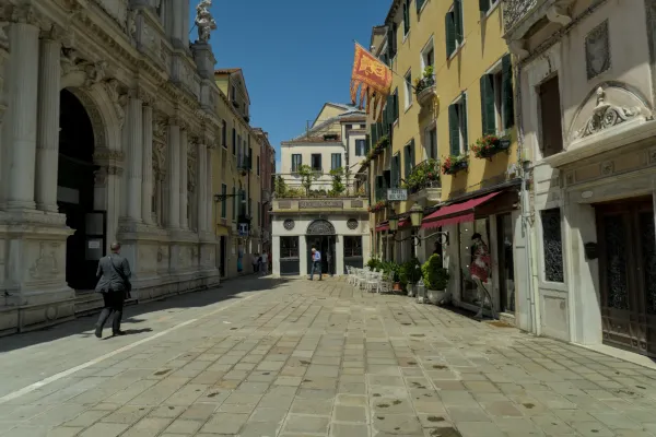 Popločana ulica u Veneciji sa istorijskim zgradama, čovekom u odelu i crvenom zastavom.