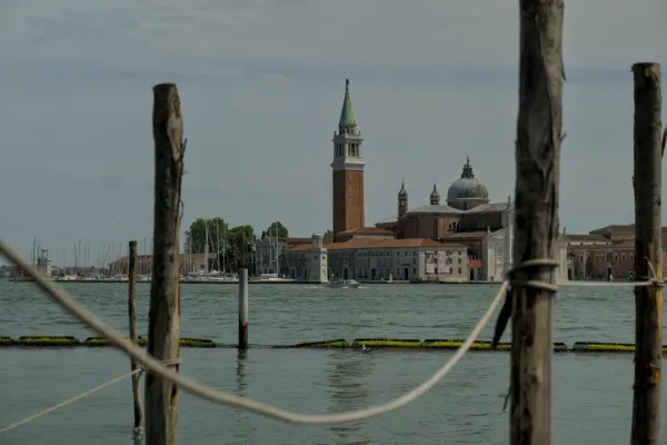 Blick über das Wasser auf die Kirche San Giorgio Maggiore und ihren Glockenturm in Venedig, eingefangen durch Holzpfähle und Seile.