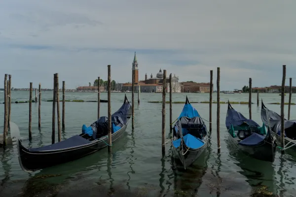 Drei Gondeln liegen vertäut an Holzpfählen vor der Skyline von Venedig mit einem markanten Glockenturm.